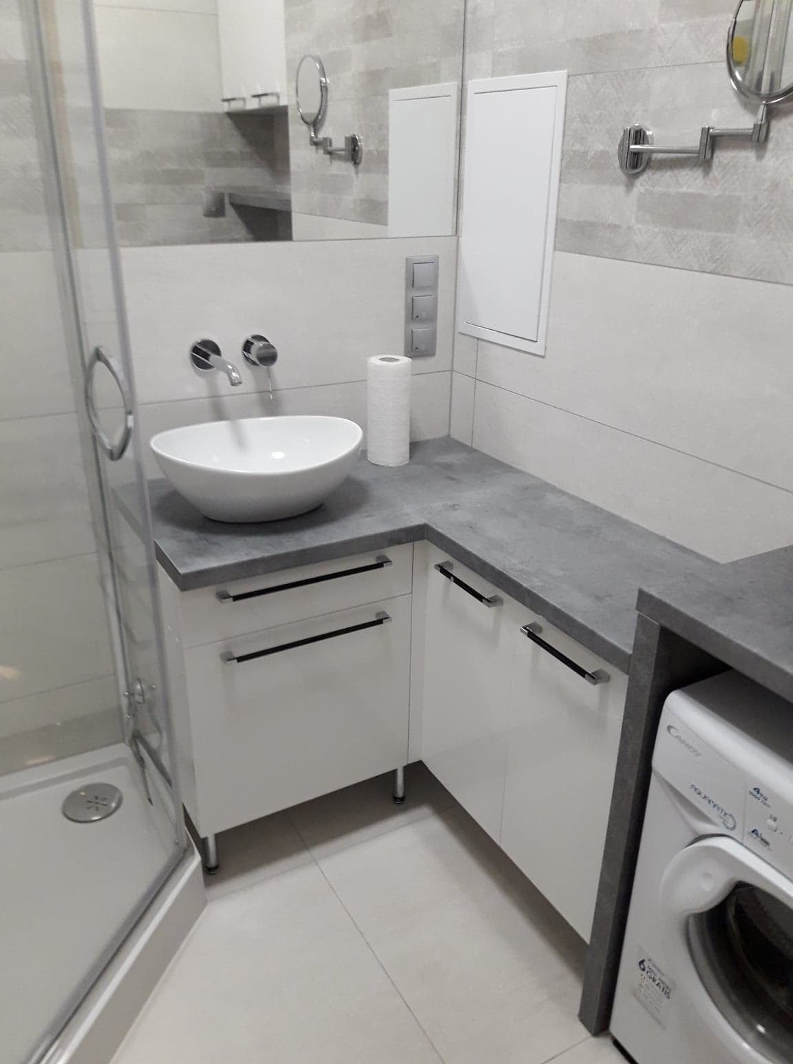 Nowoczesna łazienka z białą umywalką nablatową, szarą armaturą i blatem. W tle widoczne lustro i kabina prysznicowa. Minimalistyczny design.