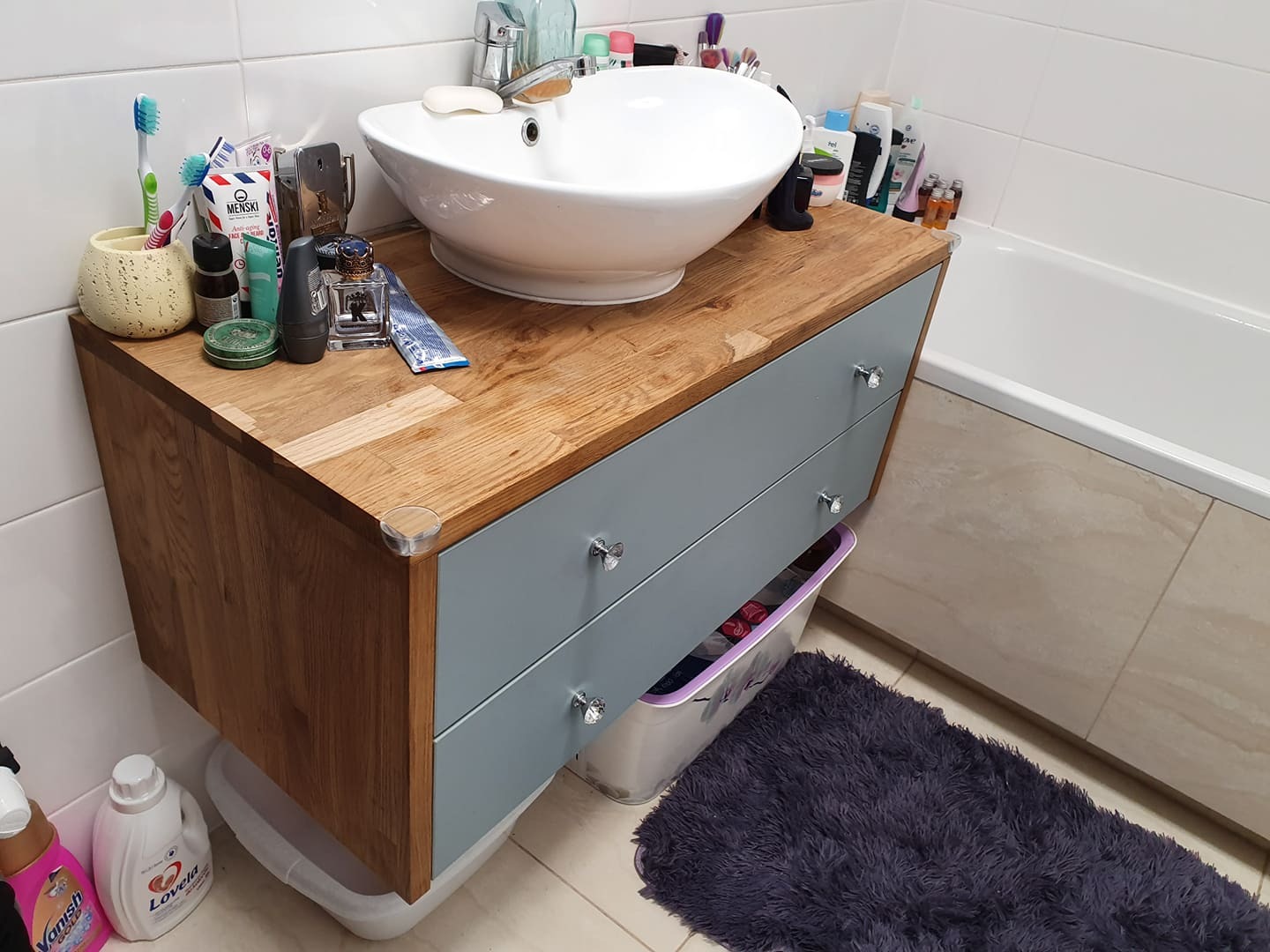 Nowoczesna łazienka: umywalka nablatowa na drewnianym blacie z szufladami w odcieniach szarości, z dodatkami kosmetycznymi i akcesoriami.