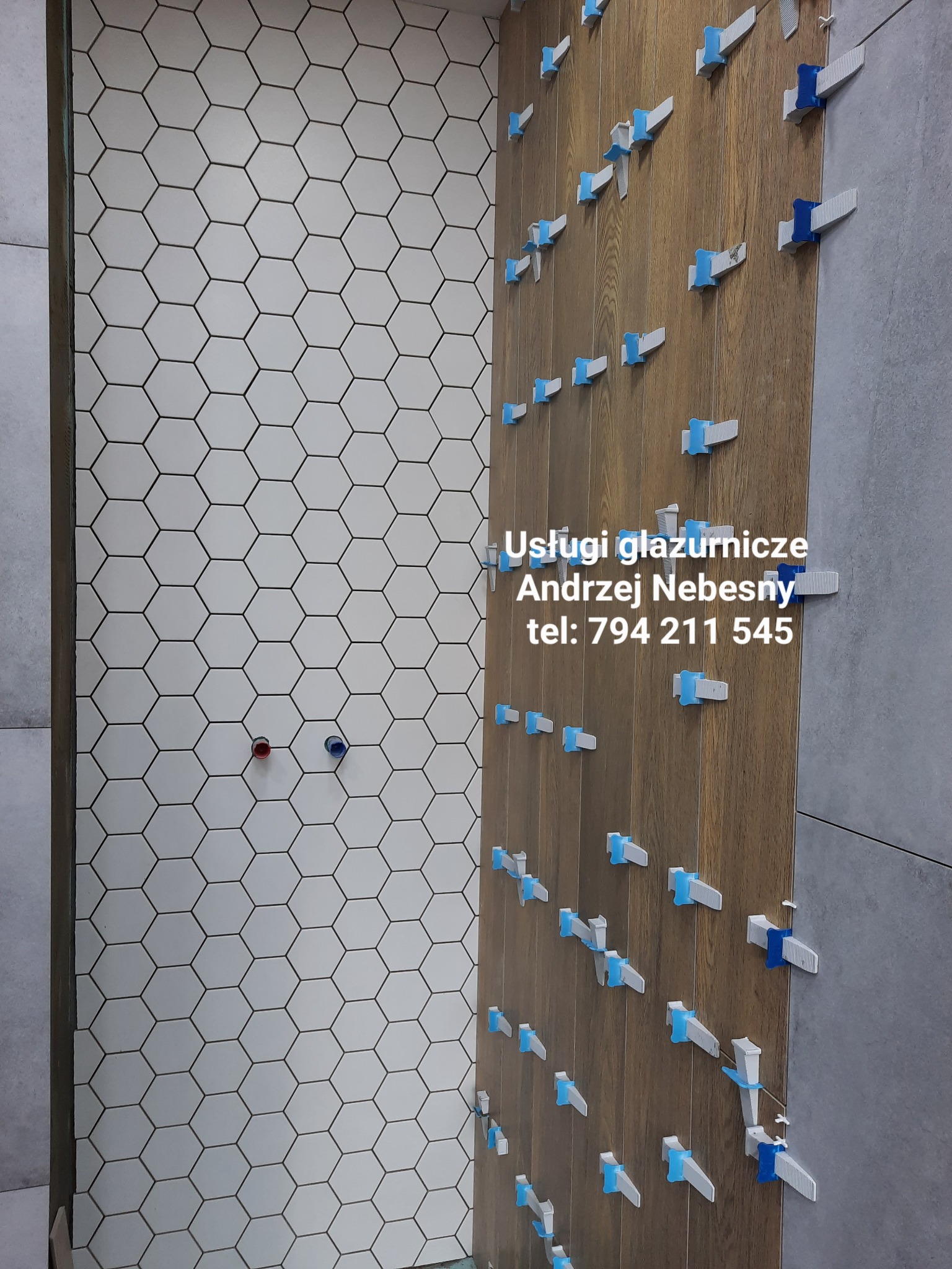 Układanie białych, heksagonalnych płytek na ścianie, widoczne niebieskie i białe klipsy poziomujące, fragment ściany z płytek imitujących drewno i szare płytki.