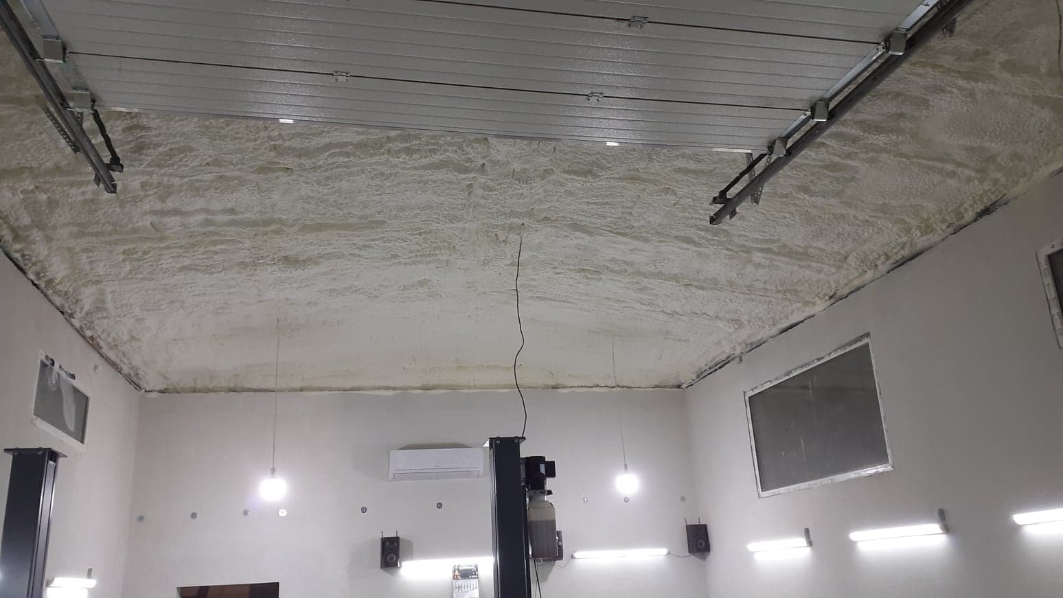 Izolacja pianką poliuretanową (PUR) natryskiwana na sufit w garażu w Somiance, widoczne elementy konstrukcyjne sufitu i oświetlenie.