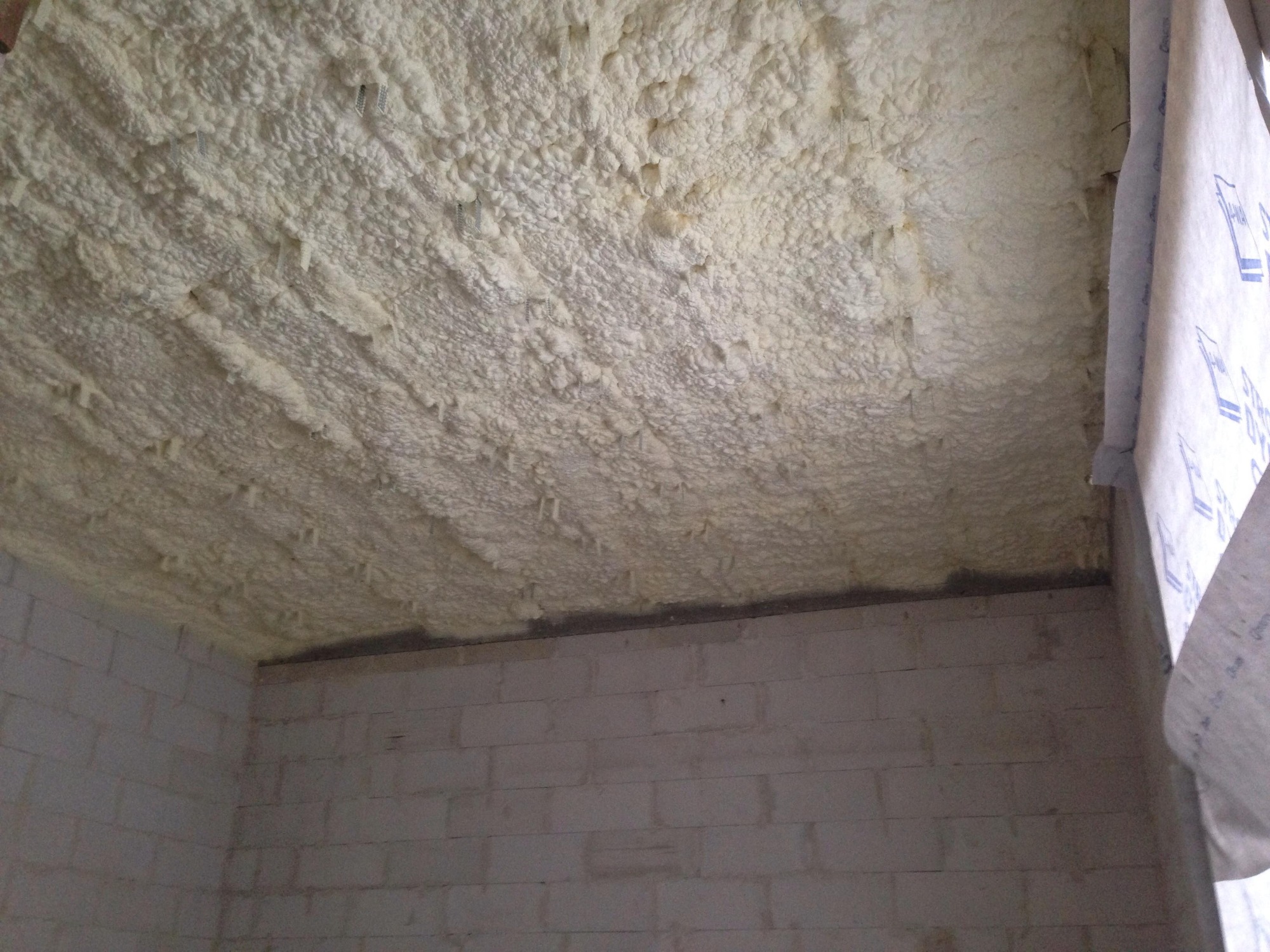 Poddasze po natrysku pianki poliuretanowej, widoczne nierówności i struktura izolacji, ściany z białego bloczka betonowego.