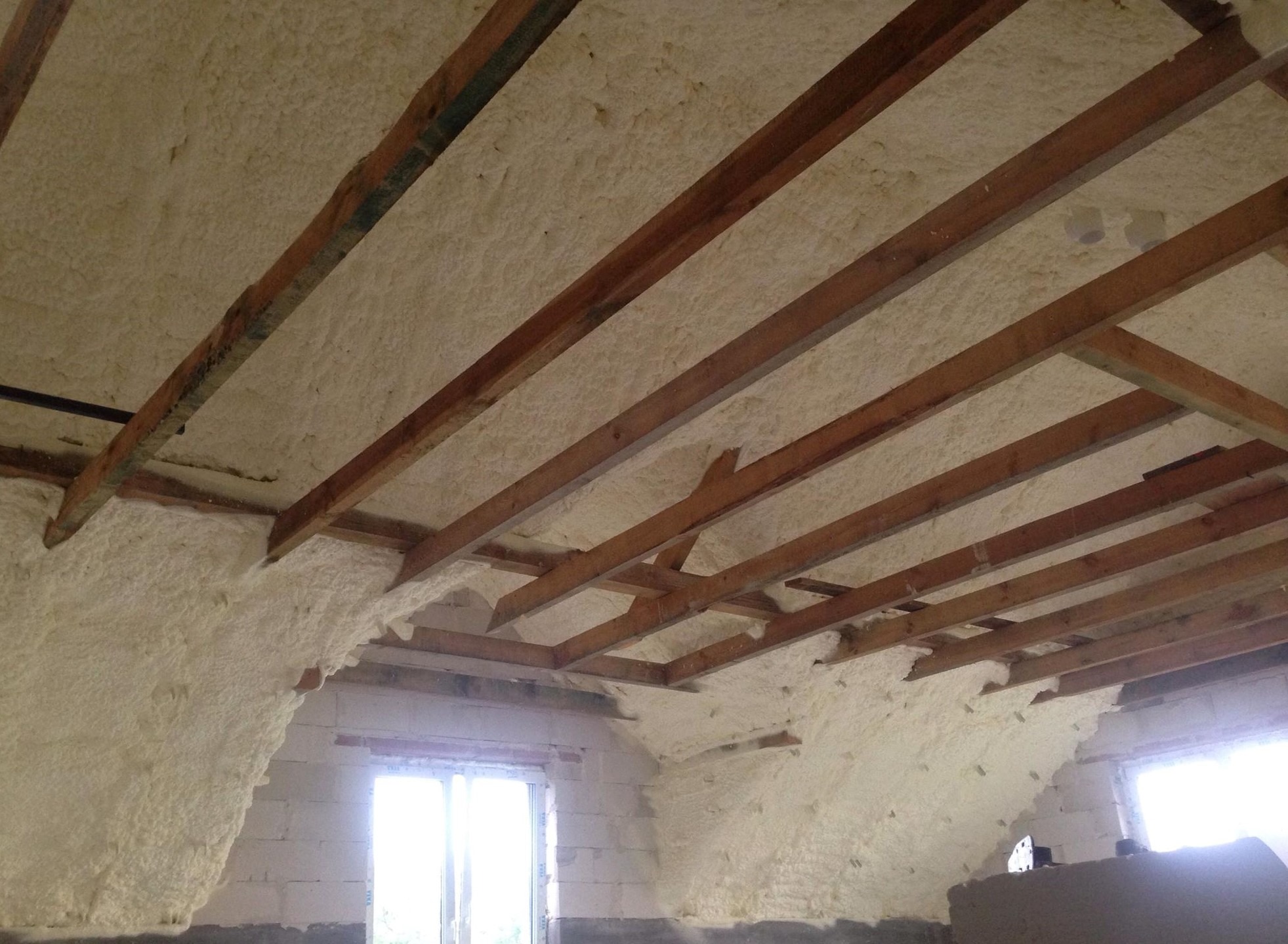 Poddasze z drewnianą konstrukcją dachu, ocieplone pianką natryskową, widok na okno dachowe.