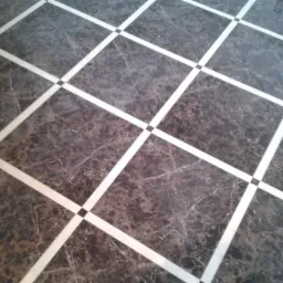 Ciemna marmurowa podłoga z białymi fugami tworzącymi wzór kraty i czarnymi kwadratami w miejscach przecięcia.