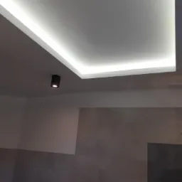 Sufit podwieszany z oświetleniem LED wzdłuż krawędzi, uzupełniony punktowym reflektorem w minimalistycznej łazience z szarymi płytkami.