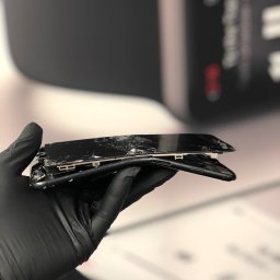 AppleFix.pl - serwis Apple Wrocław, iPhone, iPad & MacBook - Smartfon z rozbitym ekranem, trzymany w dłoni w czarnej rękawiczce ochronnej, widoczne uszkodzenia mechaniczne obudowy i wyświetlacza.