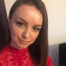 Portret kobiety w czerwonej koronkowej bluzce z długimi, ciemnymi włosami, patrzącej w obiektyw z delikatnym uśmiechem.