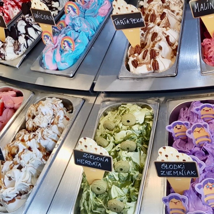 Szeroki wybór lodów w metalowych kuwetach: lody jednorożec z naklejkami jednorożców, tarta pekan, zielona herbata z ciasteczkami matcha, słodki ziemniak z dekoracjami pszczółek, malinowe i inne smaki.