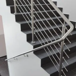 Schody z ciemnymi stopniami i nowoczesną balustradą ze stali nierdzewnej z poziomymi wypełnieniami, mocowaną do ściany i stopni.