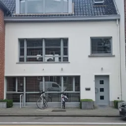 Odnowiona, biała elewacja dwukondygnacyjnego domu z szarymi oknami i drzwiami, widok z ulicy, rowery zaparkowane przed budynkiem.