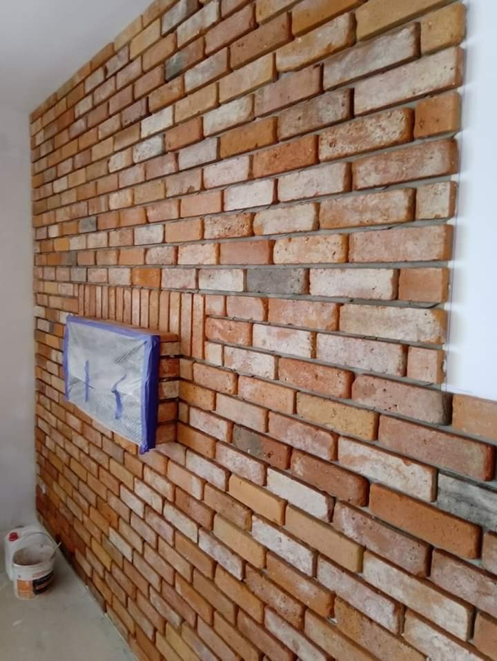 Ściana z cegły klinkierowej w trakcie montażu w Inowrocławiu, z widocznym zabezpieczonym fragmentem ściany i wiaderkiem po kleju na podłodze.