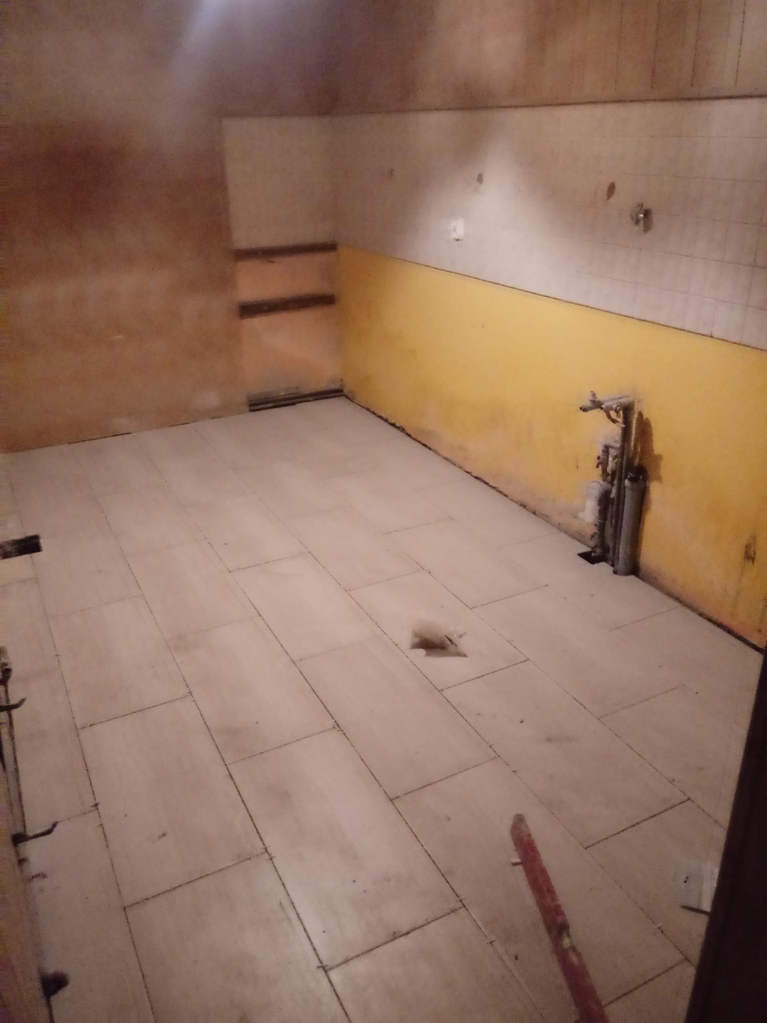 Wnętrze w trakcie remontu: ułożona jasna terakota na podłodze, fragment żółtej ściany z instalacją hydrauliczną, surowa ściana z widocznymi śladami po pracach wykończeniowych.