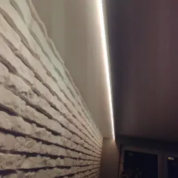 Sufit wykończony gladzią oraz kamień dekoracyjny na scianie, ozdobiony listwą LED.