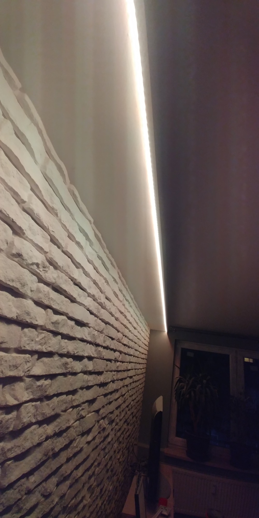 Sufit wykończony gladzią oraz kamień dekoracyjny na scianie, ozdobiony listwą LED.