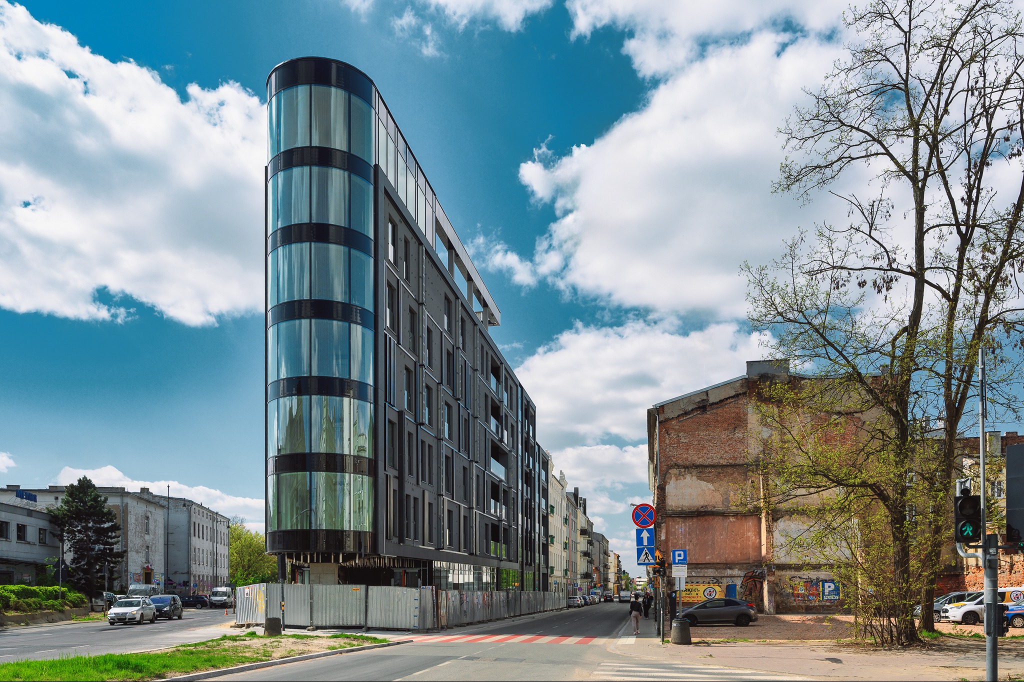 Nowoczesny budynek biurowy z zaokrągloną, przeszkloną fasadą, widoczny z poziomu ulicy w słoneczny dzień.