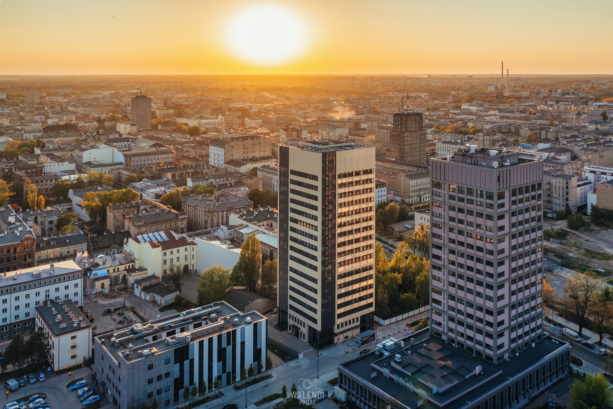 Panorama miasta z lotu ptaka o wschodzie słońca, na pierwszym planie wysokie budynki biurowe z charakterystyczną architekturą.
