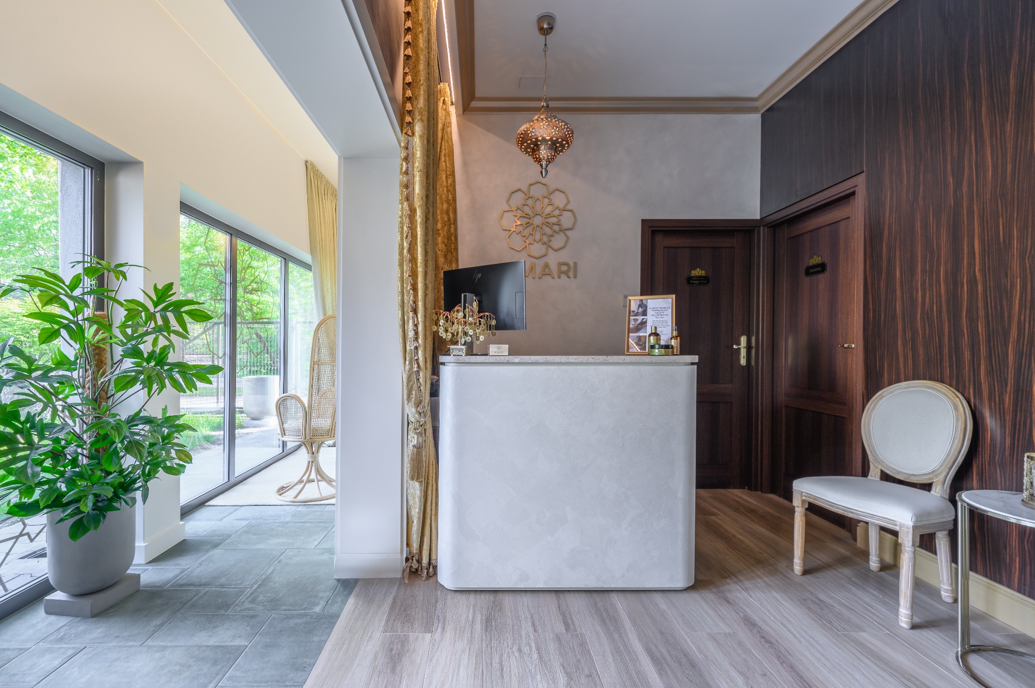 Jasne, eleganckie wnętrze z recepcją, dekoracyjną lampą i roślinami, widok na ogród przez przeszklone drzwi