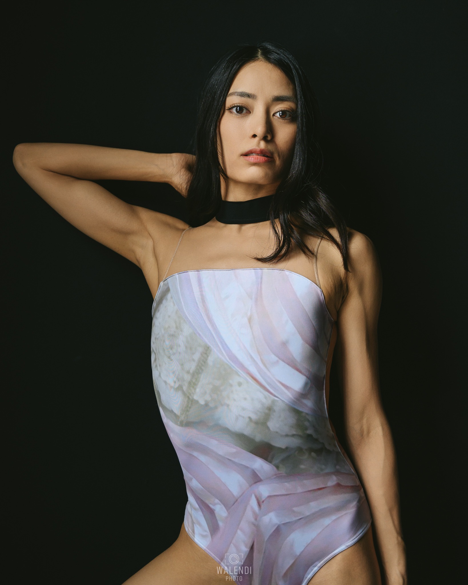 Portret kobiety w body z abstrakcyjnym wzorem, czarny choker na szyi, na ciemnym tle.