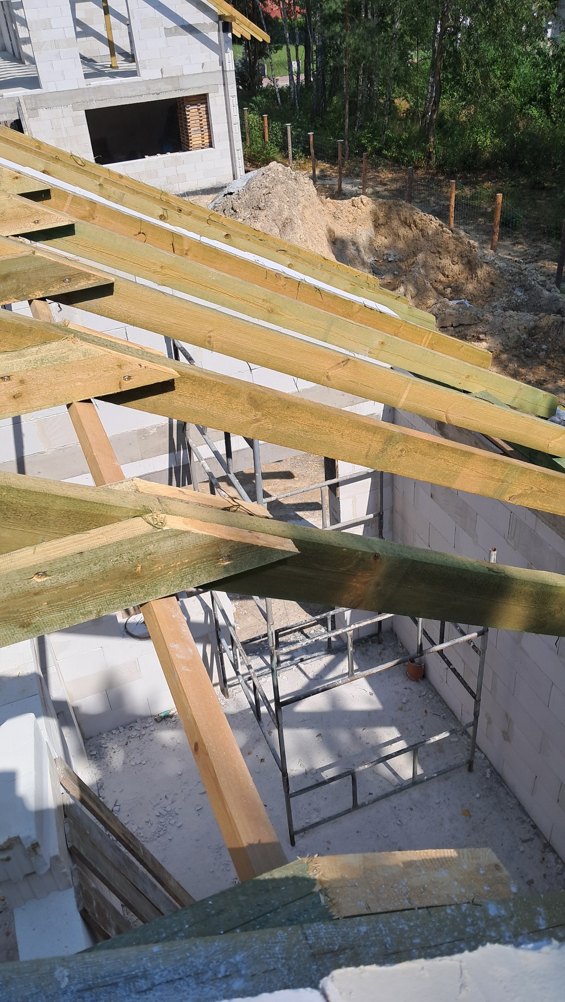 Konstrukcja drewniana więźby dachowej na powstającym domu z białych bloczków, widok z góry, rusztowanie wewnątrz budynku.