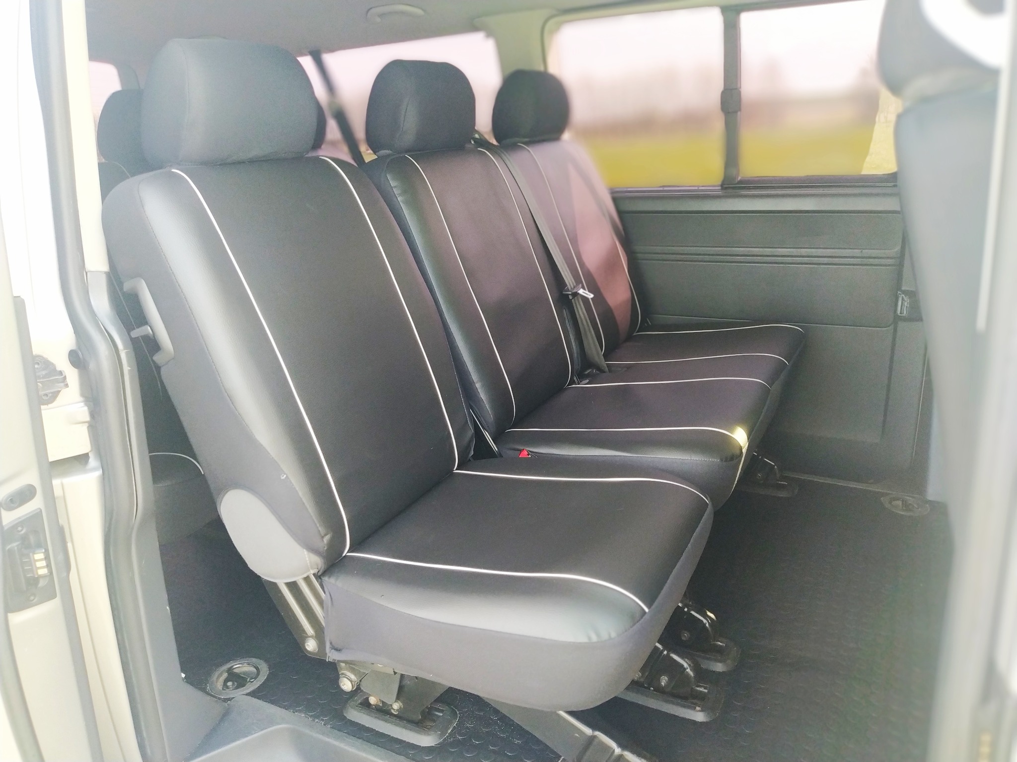 Wnętrze busa z trzema czarnymi fotelami obitymi skórą ekologiczną i obszytymi białą lamówką, widoczne mocowania foteli w podłodze.