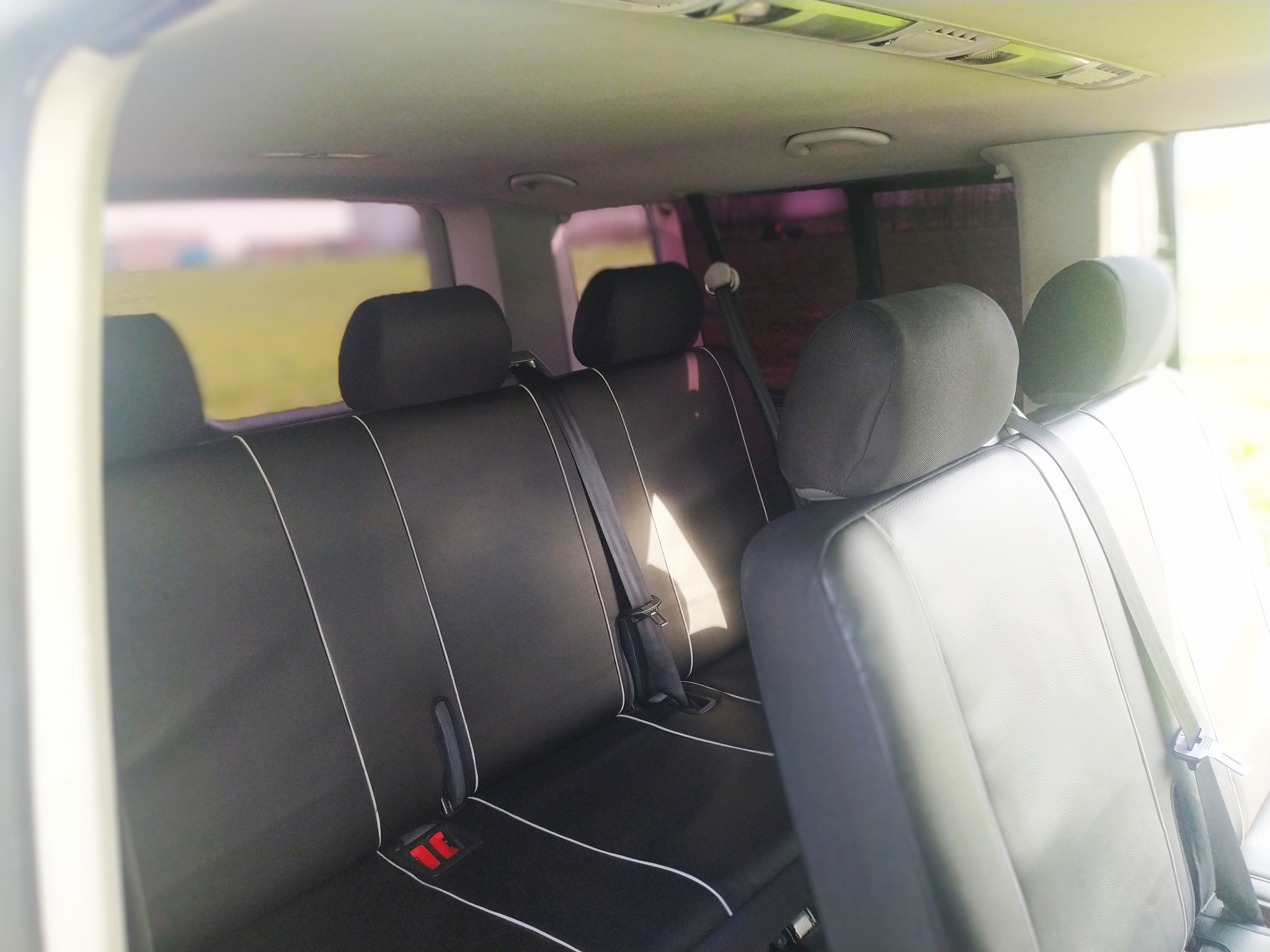 Wnętrze busa z nowymi, czarnymi pokrowcami na siedzeniach, wykończonymi białą lamówką, widoczne pasy bezpieczeństwa.