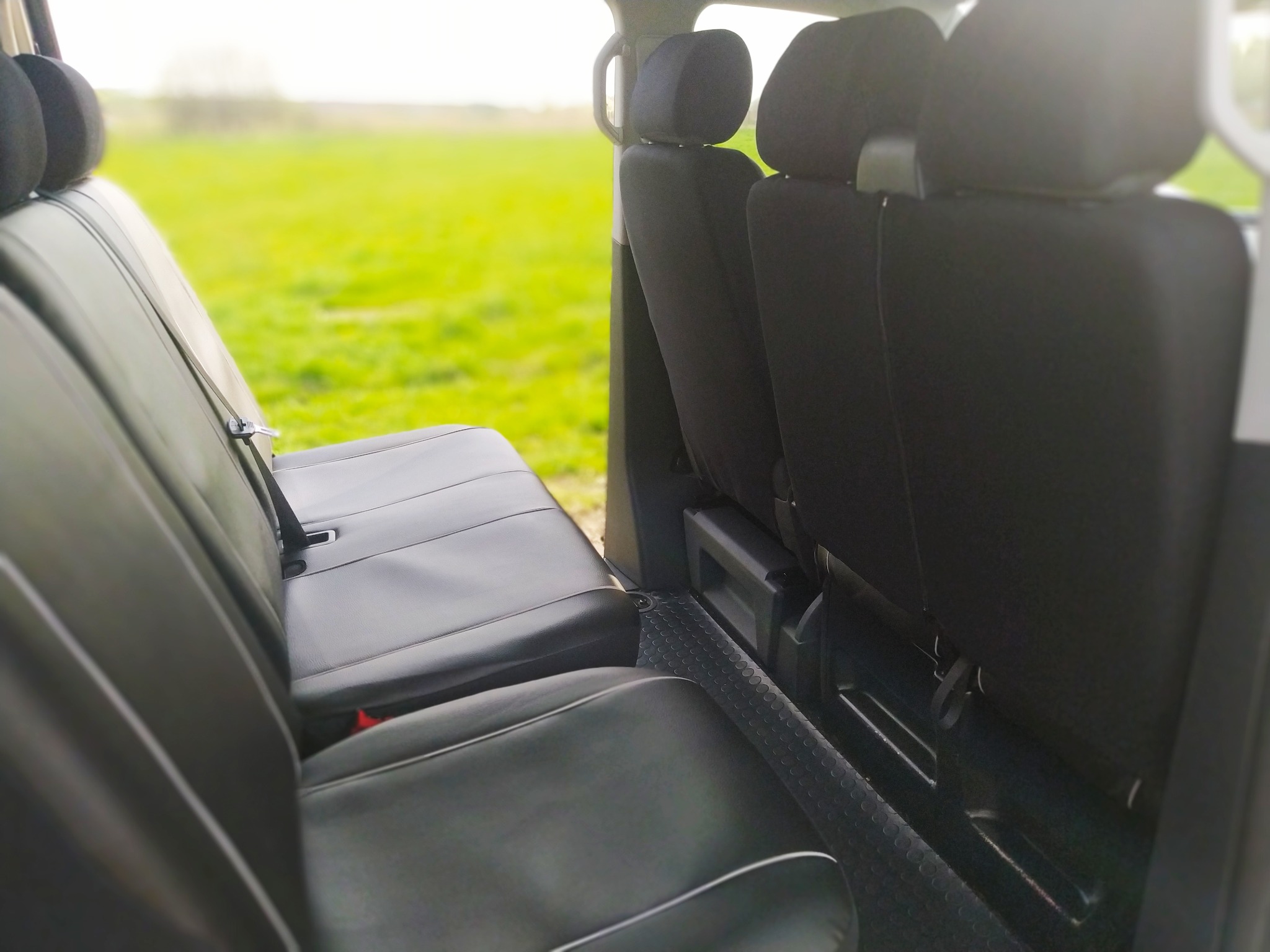 Wnętrze busa z czarnymi siedzeniami i widokiem na zielone pole za oknem, z perspektywy tylnych siedzeń.