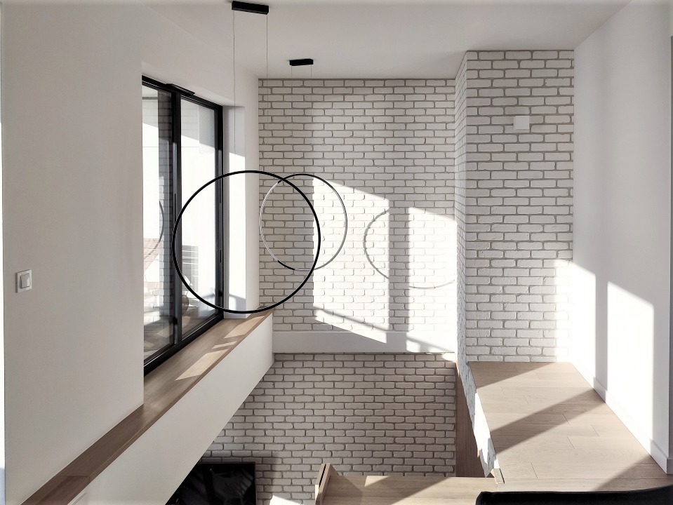 Nowoczesne wnętrze z białej cegły z designerskimi lampami wiszącymi w kształcie okręgów, widok z góry na schody z drewnianymi stopniami.