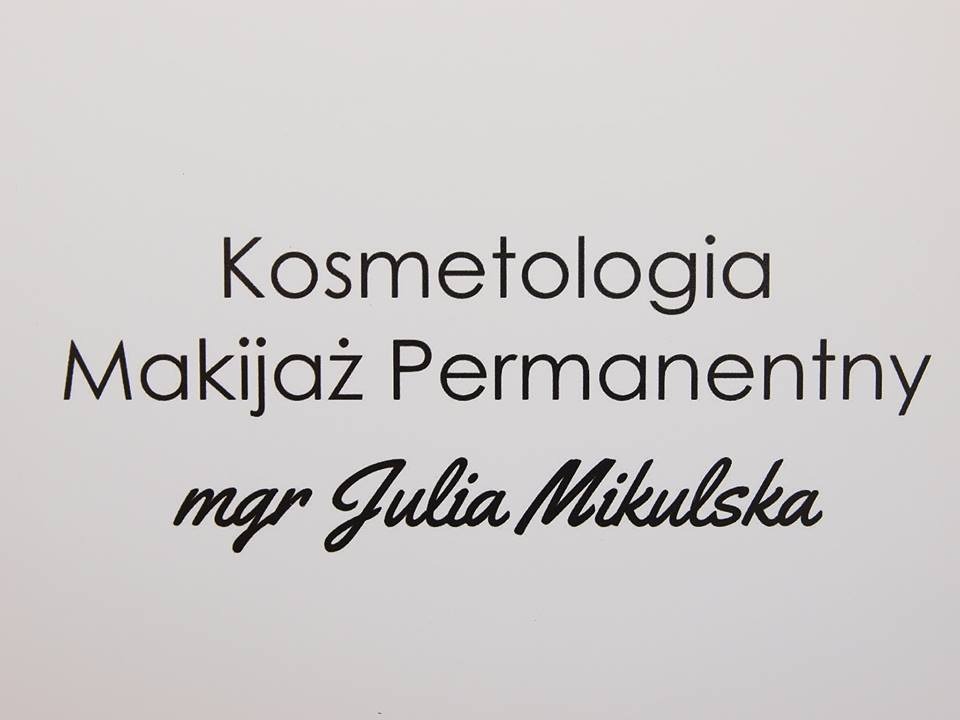 Tablica informacyjna z napisem 'Kosmetologia Makijaż Permanentny mgr Julia Mikulska' czarną czcionką na białym tle.