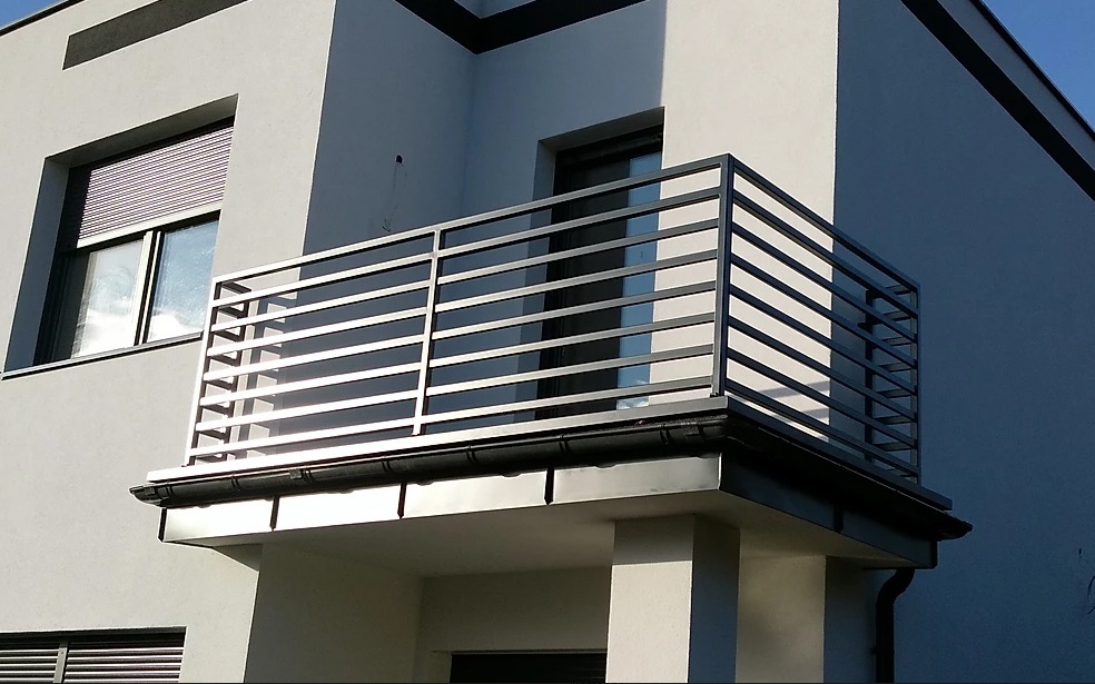 Nowoczesna balustrada balkonowa z poziomych, metalowych profili na tle minimalistycznej elewacji budynku.