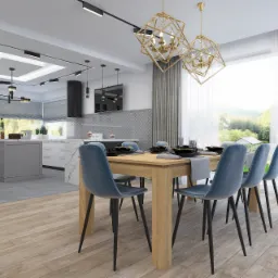 Jasna jadalnia z drewnianym stołem, krzesłami w odcieniach błękitu i złotymi, geometrycznymi lampami wiszącymi, widok na kuchnię z szarą wyspą i okapem.
