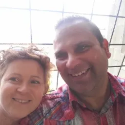 Uśmiechnięta para robi selfie na tle okna z kratami i widokiem na zieleń za oknem.