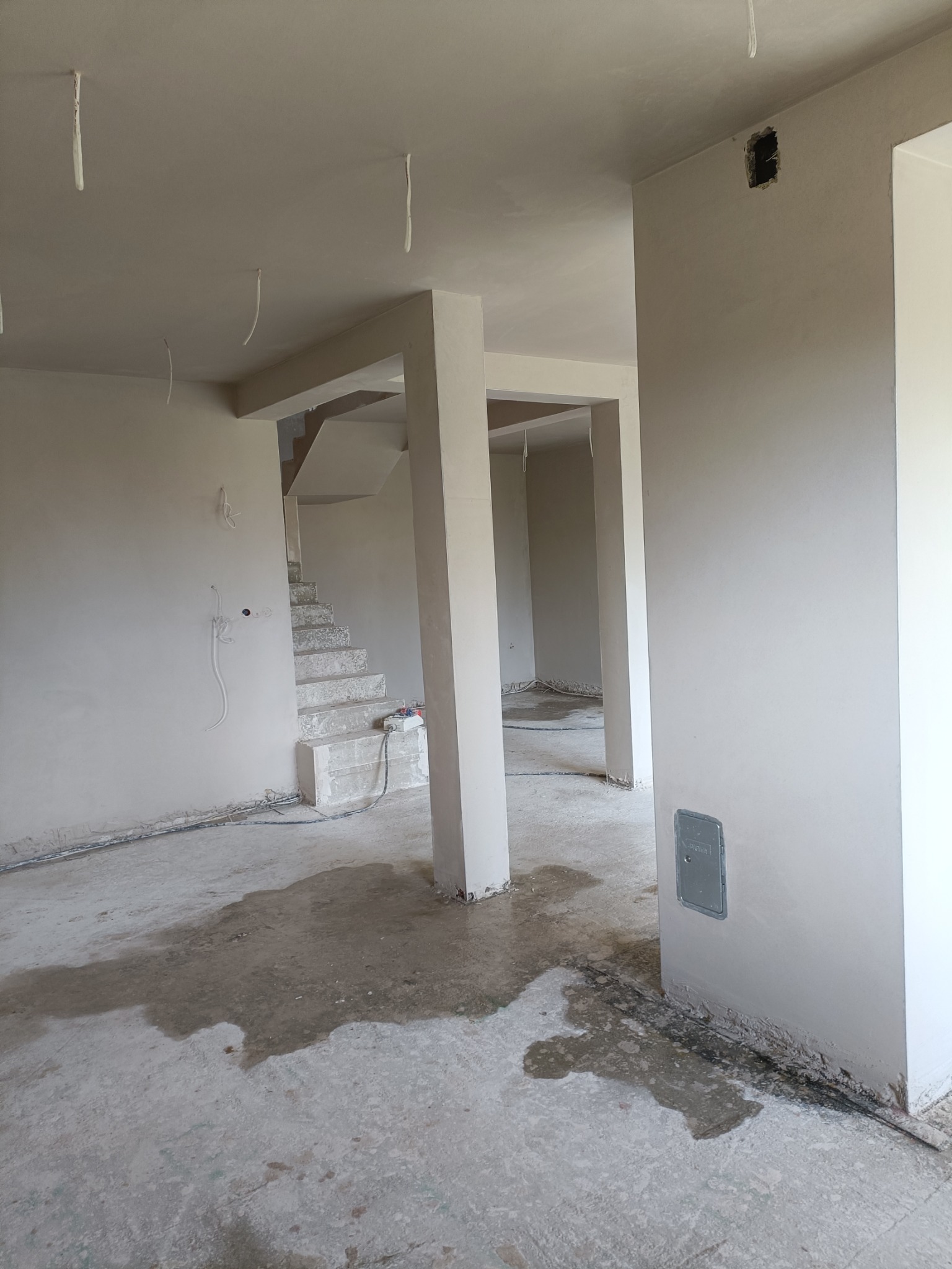 Wnętrze po tynkowaniu maszynowym: gładkie ściany, surowe schody, widoczne kable i instalacje. Stan surowy, przygotowanie do dalszych prac wykończeniowych.