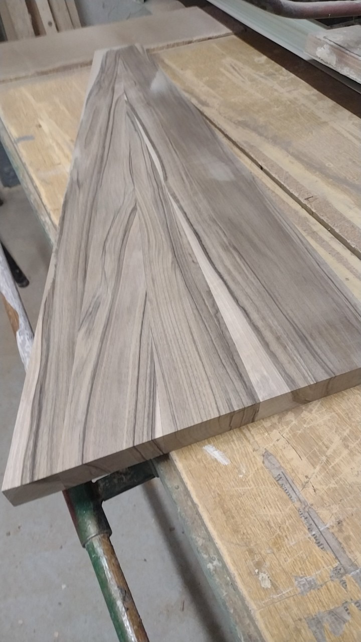 Kawałek drewna o unikalnym wzorze słojów, leżący na roboczym stole z widocznymi śladami użytkowania.