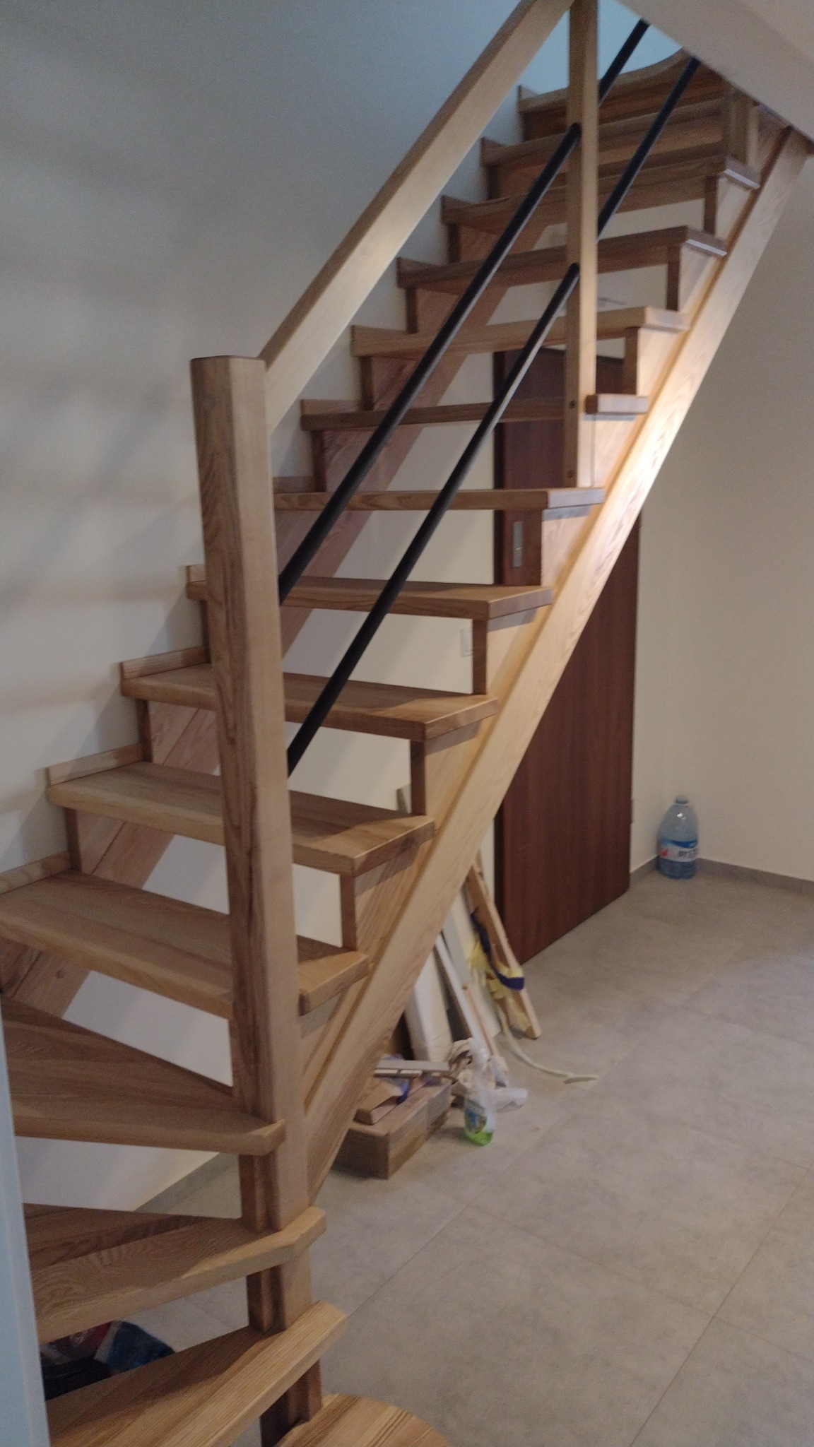 Drewniane schody z czarnymi metalowymi balustradami zamontowane w jasnym wnętrzu, widoczne ślady prac wykończeniowych na podłodze.