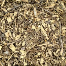 Zrębki drzewne z widocznymi fragmentami kory i gałązek, o zróżnicowanej kolorystyce od jasnego beżu po ciemny brąz, ułożone warstwowo.