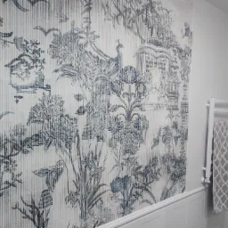 Ściana w łazience pokryta tapetą w stylu toile de jouy z motywem pawia i roślinności, biała grzejnik drabinkowy z szarą ręcznikiem w romby.