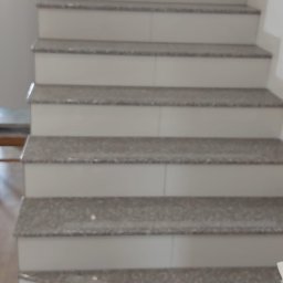 Bud-Mar Marcin Kołtonowski - Wykończone schody wewnętrzne z szarymi, błyszczącymi płytkami imitującymi kamień, białe podstopnice, widok z dołu na górę.