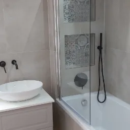 Nowoczesna łazienka z beżowymi płytkami, kabiną prysznicową z dekoracyjnymi wstawkami, białą umywalką nablatową i podświetleniem LED pod szafką umywalkową.