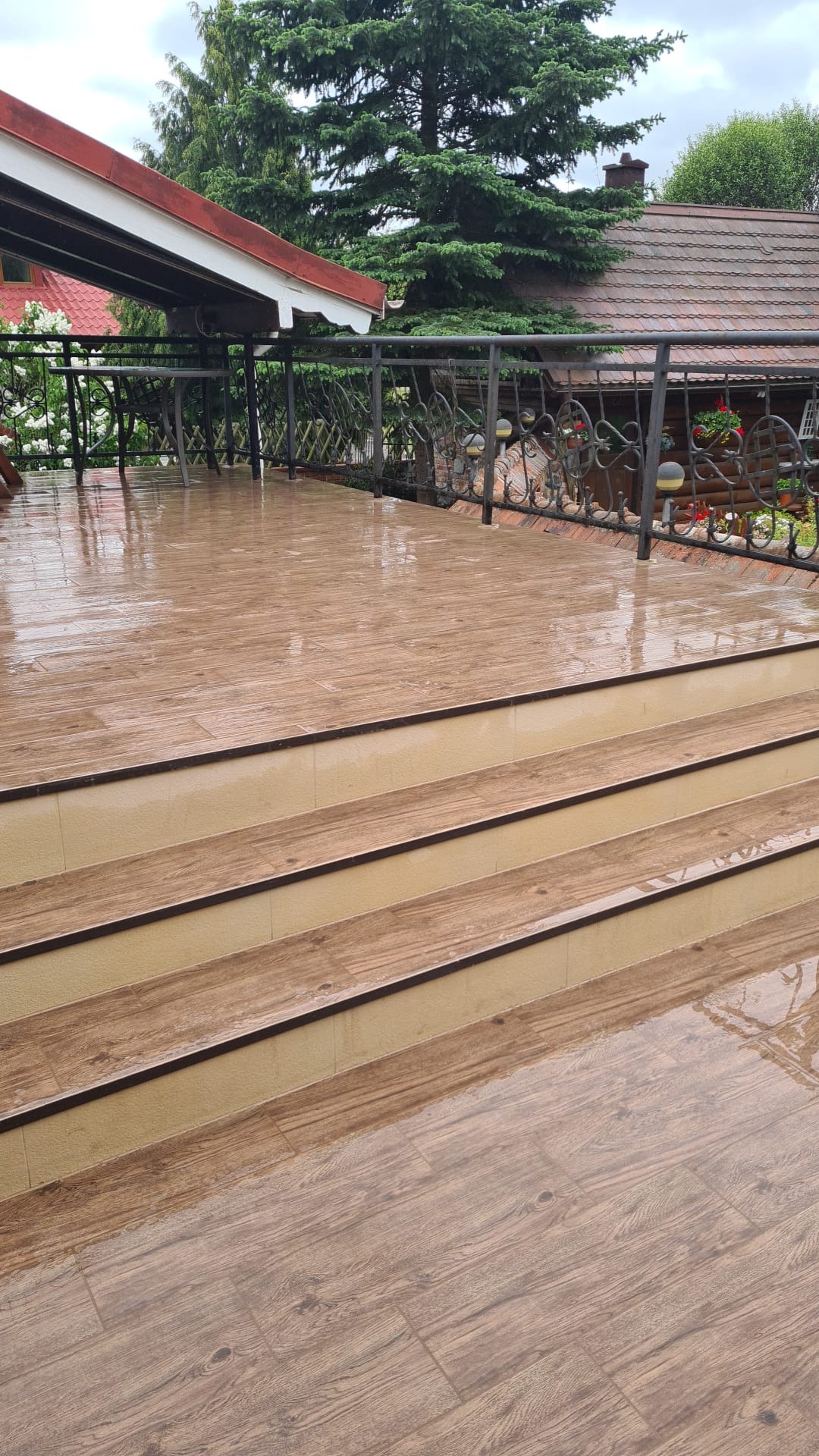 Wyłożony płytkami taras z balustradą w Gniewie, mokry po deszczu, z widocznymi schodami i fragmentem zadaszenia.