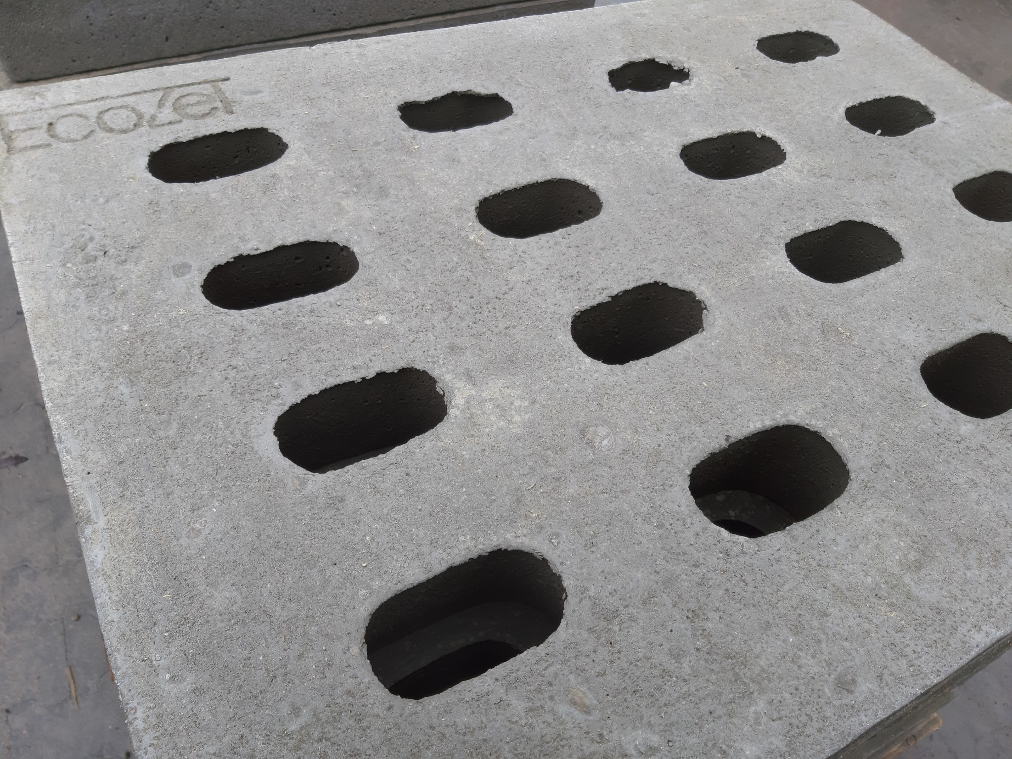 Szara, betonowa płyta z podłużnymi otworami, widoczny napis 'Ecozel'.