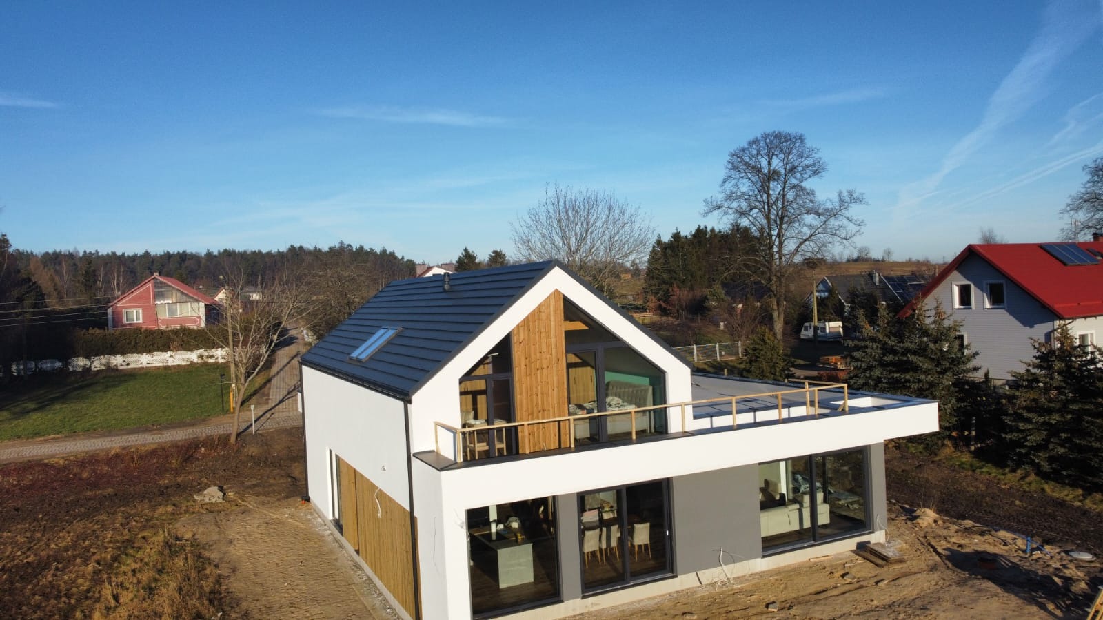 Nowoczesny dom z białymi ścianami, drewnianymi elementami fasady i płaskim dachem z tarasem, widok z lotu ptaka.