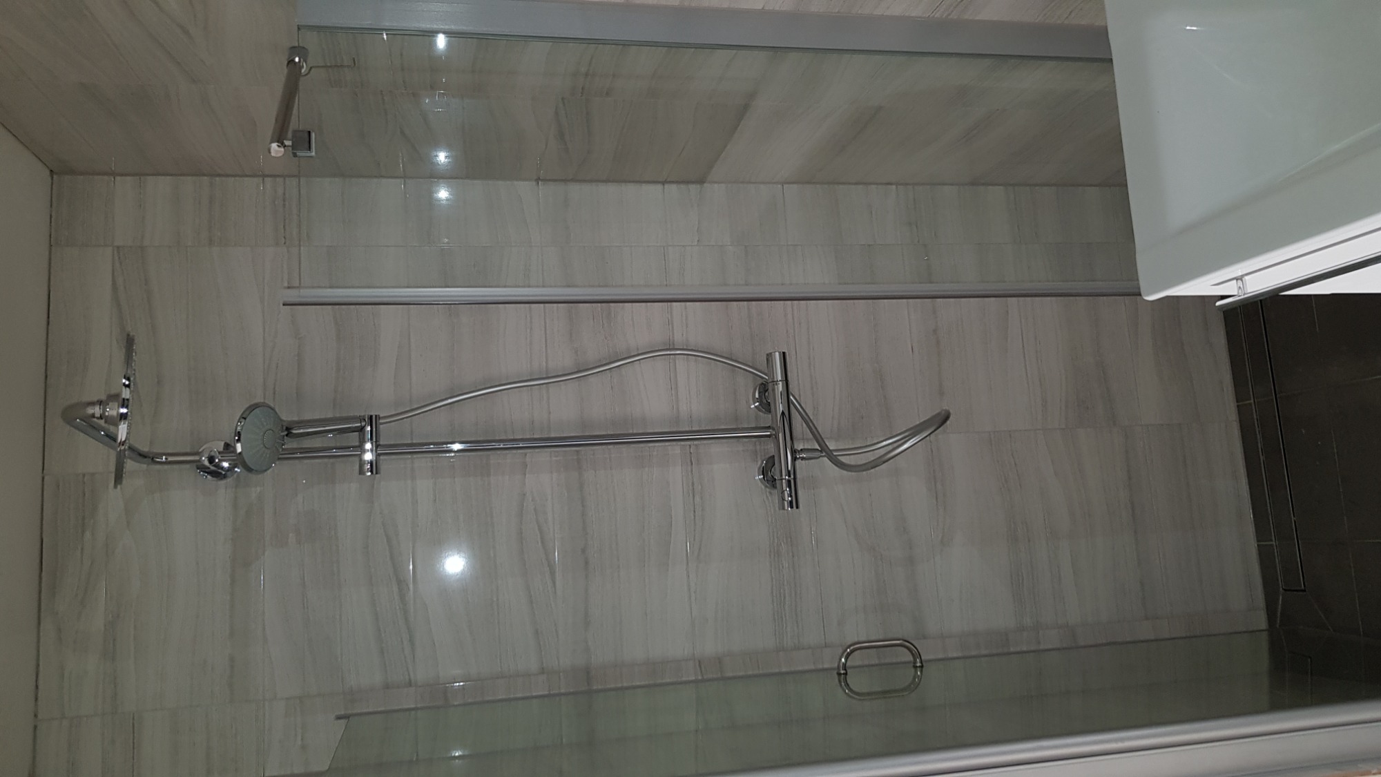 Nowoczesna kabina prysznicowa z szarymi płytkami imitującymi marmur, wyposażona w deszczownicę i zestaw prysznicowy, widoczny odpływ liniowy.