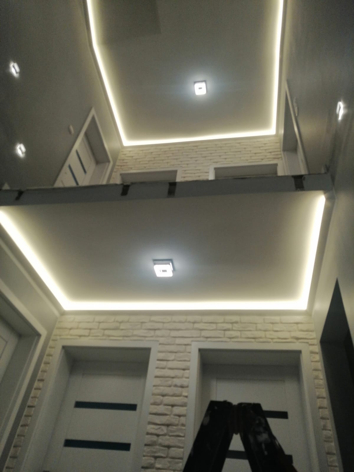 Korytarz z podwieszanym sufitem i oświetleniem LED, widok z dołu, biała cegła na ścianach, drabina w kadrze.