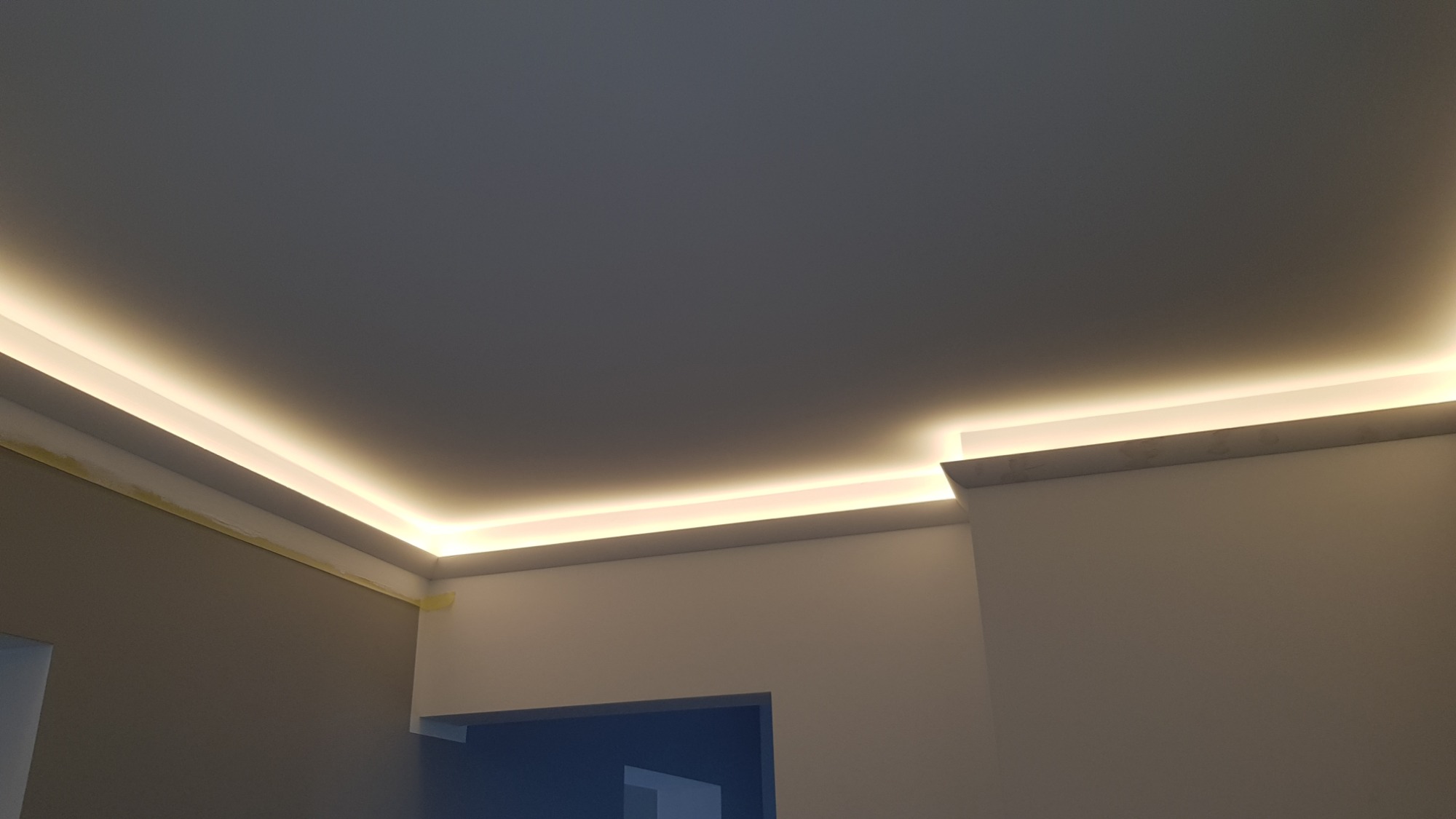 Sufit z oświetleniem LED w ukrytej listwie, widoczne fragmenty ścian, w tle widoczne drzwi.