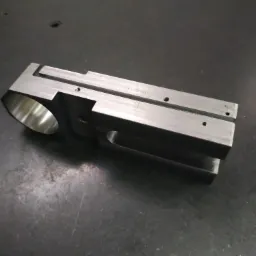 Precyzyjnie obrobiony, metalowy element z otworem i rowkami, leżący na ciemnej, metalowej powierzchni roboczej.