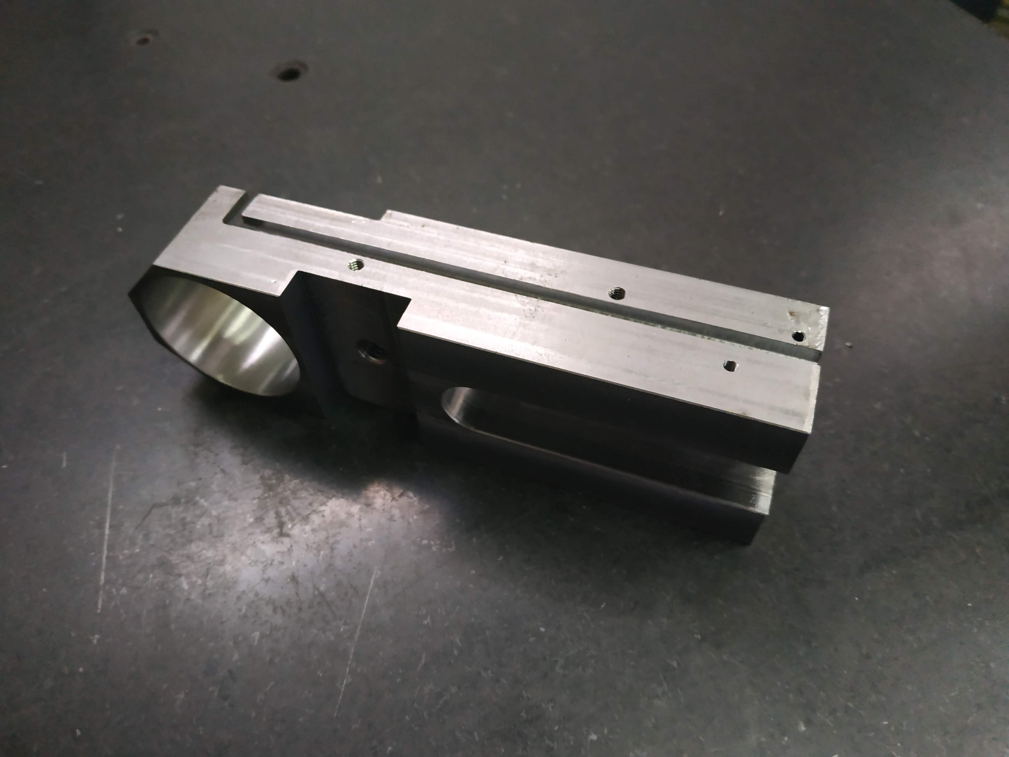 Precyzyjnie obrobiony, metalowy element z otworem i rowkami, leżący na ciemnej, metalowej powierzchni roboczej.