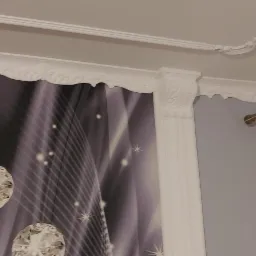 Dekoracyjna listwa sufitowa z ornamentami, kolumna dekoracyjna z motywem liści, oraz zasłona z motywem diamentów w nowoczesnym wnętrzu.