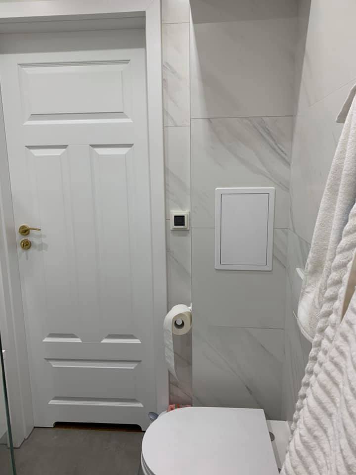 Wykończona łazienka w Rabce-Zdroju z białą armaturą, marmurkowymi płytkami i białą stolarką drzwiową z akcentami w kolorze złota.