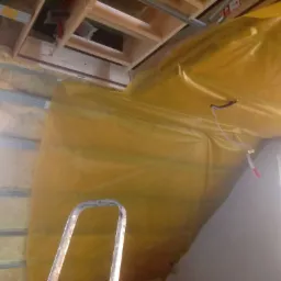 Poddasze w trakcie ocieplania: widoczna wełna mineralna między profilami, folia paroizolacyjna w kolorze żółtym zabezpieczająca izolację, oraz fragment drabiny malarskiej.