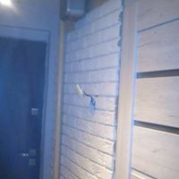 Fragment ściany z białej cegły dekoracyjnej, widoczne wystające kable elektryczne i drewniane elementy konstrukcyjne, obok ciemne drzwi.