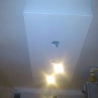 Biały, prostokątny sufit podwieszany z trzema punktami świetlnymi, widoczne niedoskonałości w wykończeniu, słaba jakość zdjęcia.